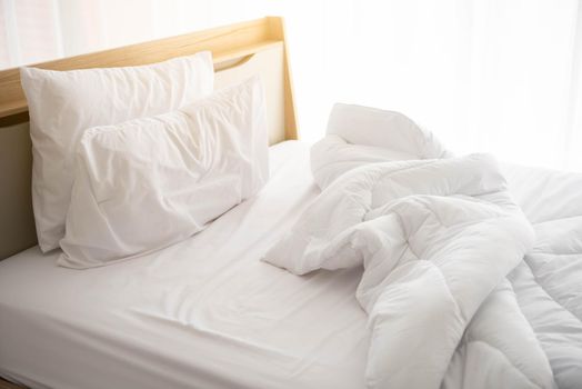 White unmade bed in the morning with sunshine with white curtain background in elegant home. Interior design and luxury furniture concept. Indoors lifestyle and Lazy activity theme.