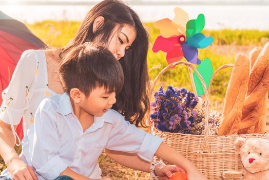 Beautiful Asian mother and son doing picnic and in Easter summer party on meadow near lake and mountain. Holiday and Vacation. People lifestyle and Happy family life concept. Thai person