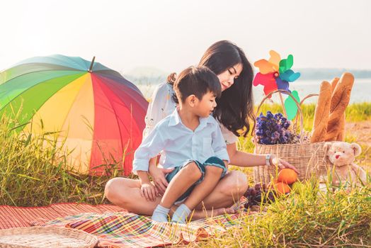 Beautiful Asian mother and son doing picnic and in Easter summer party on meadow near lake and mountain. Holiday and Vacation. People lifestyle and Happy family life concept. Thai person