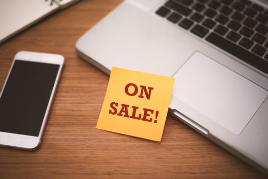 "On sale" text on post it paper near laptop and smart phone on wood table, Online shopping and Technology marketing concept. Split and cross processing tone pinterest and instragram like process.