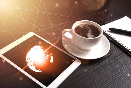 Tablet and black coffee on wooden table with Digital Earth world map and orange light and line dot, Notebook and pen, Technology concept, Drinking and Relax concept, Coffee break time concept