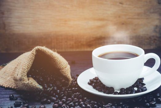 Side view of Coffee cup with  smoke and coffee beans in sack on wood table, Drinks and relax concept, for advertising