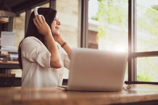 Happy Asian woman relaxing and listening music in coffee shop with computer laptop. People and lifestyles concept. Freelance and outdoors workplace outdoors theme.