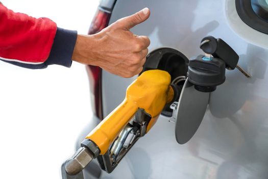 Man's hand with raised finger up, next to refueling gun, while refueling car with gasoline fuel, at gas station concept of high-quality service and fuel. Close-up.