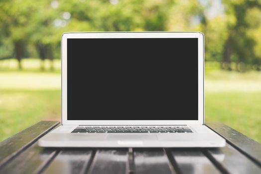 Laptop computer with blank black screen on green nature background. Natural and technology concept. Object and electronics theme. Front view angle