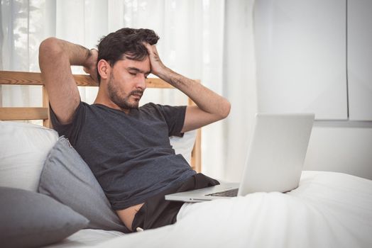 Man stressed out from work with laptop in bedroom. Technology and lifestyle concept. Social issues and problem. Healthcare and Office syndrome. Economic downturn and Critical deadline crisis theme.
