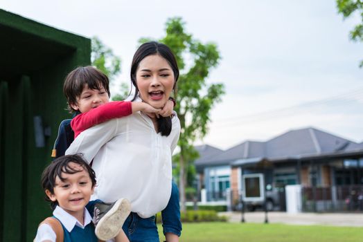 Single mom carrying and playing with her children in  garden with green wall background. People and Lifestyles concept. Happy family and Home sweet home theme. Outdoors and nature theme.