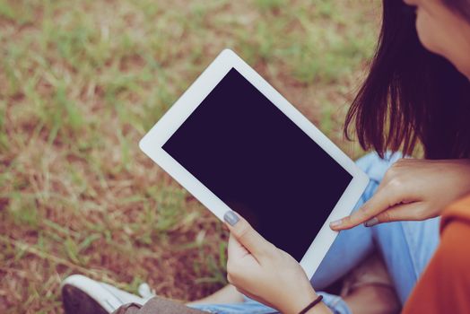 Beauty Asian woman using tablet at park. People and Technology concept. Leisure and Outdoor activity theme.