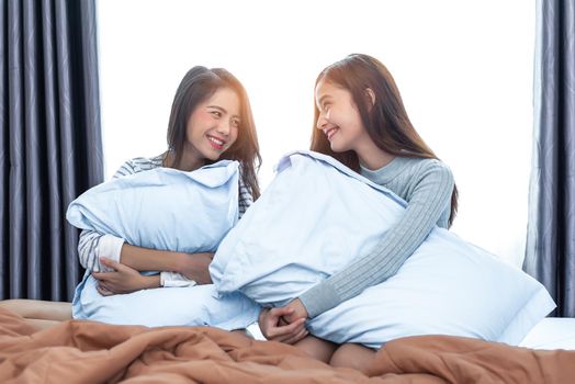 Two Asian Lesbian women looking together in bedroom. Couple people and Beauty concept. Happy lifestyles and home sweet home theme. Cushion pillow element and window background.