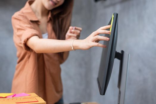 Business woman sticking order list memo on computer screen for reminding to send parcels to customers. Business and Service concept. Online shopping and Small business entrepreneur theme.