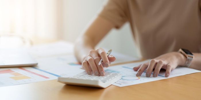 Close up woman using calculator and laptop, reading documents, young female checking finances, counting bills or taxes, online banking services.