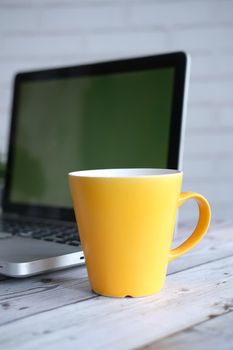 yellow color coffee mug and laptop a on table .