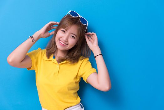 Beauty woman posing with sunglasses in front of blue wall background. Summer and vintage concept. Happiness lifestyle and people portrait theme. Cute and pastel tone.