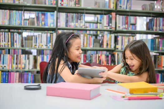 Two girls fighting for tablet in the classroom while reading books. People lifestyles and education. Young friendship and Kids relationship in school concept. Daycare and diversity theme