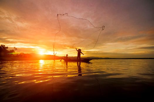 Silhouette Fisherman Fishing by using Net on the boat with sunshine in Thailand in the morning ,Nature and Culture concept