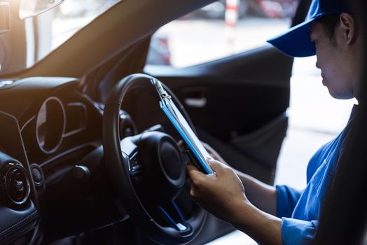 Mechanic holding clipboard and checking inside car to maintenance vehicle by customer claim order in auto repair shop garage. Repair service. People occupation and business job. Automobile technician