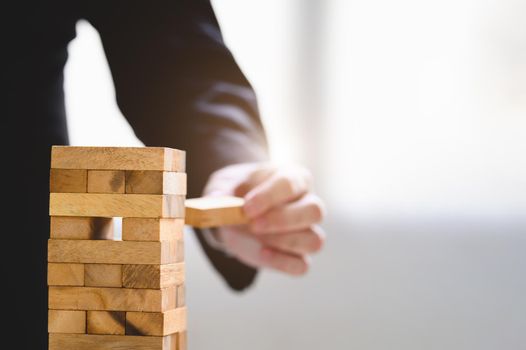 Businessman take and picking one wood block on stacked tower by hand as startup project. Business organization and company growth progress. Success of strategy and money investment. Risk management