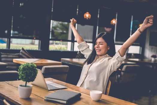 Beauty Asian woman raising two hands after finishing job happily with laptop computer. People and lifestyles concept. Technology and Business working theme. Occupation and coffee shop theme.