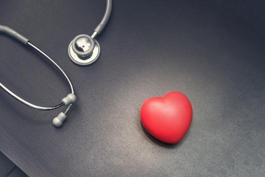 in top view, Red heart with stethoscope medical equipment on the doctor desk background. Medical and Health care concept, Hospital and Emergency theme, Dark tone pinterest and instragram like process.