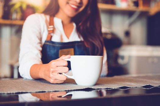 Closeup of white coffee cup with beautiful Asian woman barista background for serving to customer. Job and occupation. Food and drink beverage. Coffee shop and Cafe. Business and restaurant ownership