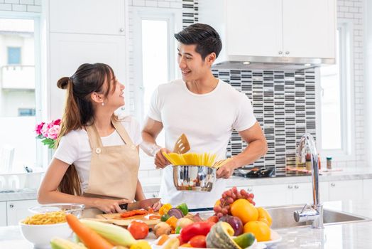 Happy Asian young married couple prepare for making spaghetti bolognese in kitchen. Boyfriend and girlfriend cooking together. People lifestyle and romantic relationship concept. Valentines day indoor