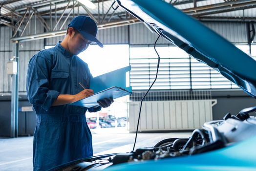 Car mechanic holding clipboard and checking to maintenance vehicle by customer claim order in auto repair shop garage. Engine repair service. People occupation and business job. Automobile technician