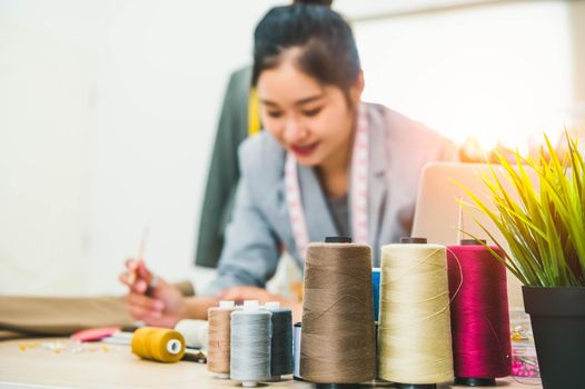 Closeup of color thread with blurry happy female tailor and sewing clothing stylist designer background. Woman creating new collection in workshop office. People lifestyle and freelance occupation job