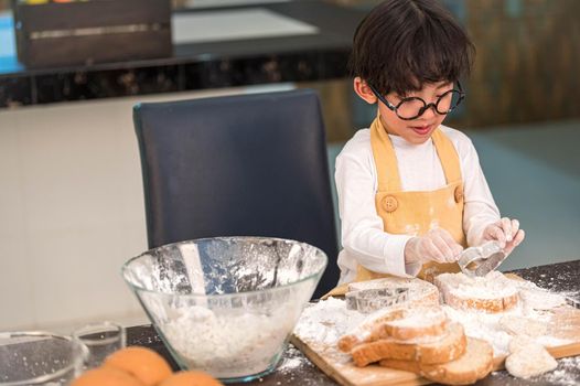 Portrait cute little Asian happiness boy interested in baking bakery with funny in home kitchen. People lifestyles and Family. Homemade food and ingredients concept. Baking Christmas cake and cookies