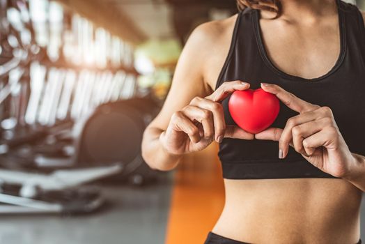 Happy sport woman holding red heart in fitness gym club. Medical cardio heart strength training lifestyle. Pretty female sport girl workout exercise. Cardiac healthy and well-being. Massage ball in hand