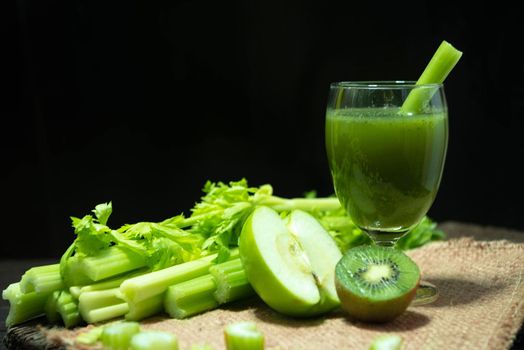 Blended mixed juice Celery and Kiwi and Green apple in welcome drink glass and bunch of fresh celery stalk on wooden table with leaves on black background. Food and ingredients  of healthy vegetable.