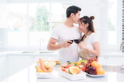Asian lovers in kitchen, Man give forehead kiss to woman while clink wine glasses to each other. Family and Couple concept. Honeymoon and Holidays theme