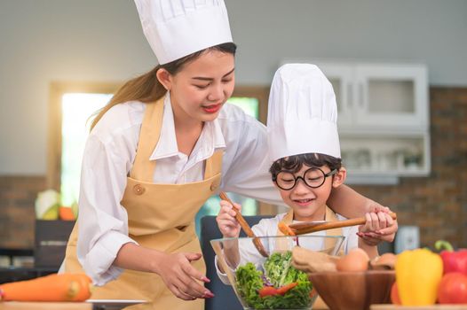 Happy beautiful Asian woman and cute little boy with eyeglasses prepare to cooking in kitchen at home. People lifestyles and Family. Homemade food and ingredients concept. Two Thai people life