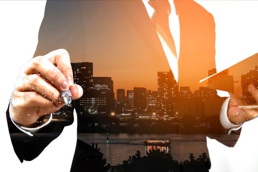 Businessman holding memo and ready to write down with big town or city in the background. Double exposure, panoramic view contemporary megalopolis background, orange sun light, business concept