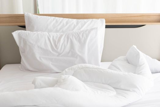 White unmade bed in the morning with sunshine with white curtain background in elegant home. Interior design and luxury furniture concept. Indoors lifestyle and Lazy activity theme.