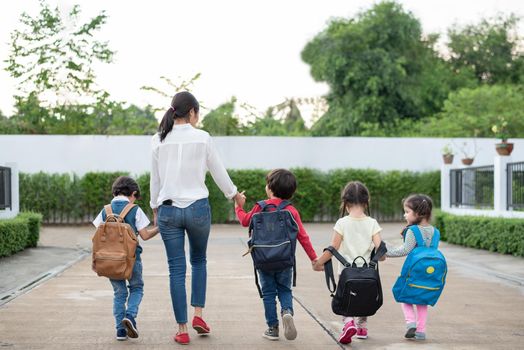 Group of preschool student and teacher holding hands and walking to home. Mom bring her children go to school together. Back to school and Education concept. People and lifestyles theme. Back view 