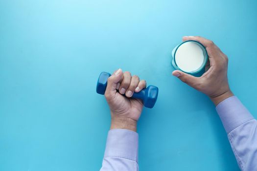 young man hand holding dumbbell and glass of milk on blue .