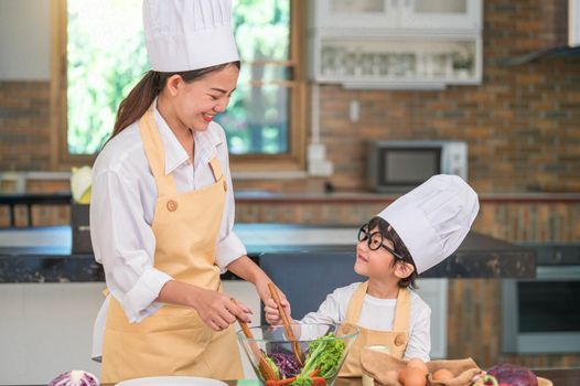 Happy beautiful Asian woman and cute little boy with eyeglasses prepare to cooking in kitchen at home. People lifestyles and Family. Homemade food and ingredients concept. Two Thai people life