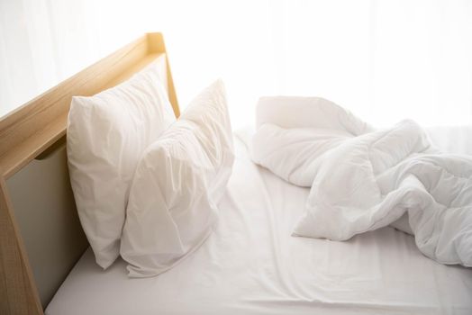 White unmade bed in the morning with sunshine with white curtain background in elegant home. Interior design and luxury furniture concept. Indoors lifestyle and Lazy activity theme.
