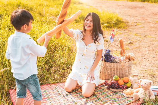 Mother and son play fencing with bread together when picnic at outdoors near lake or river. People lifestyles and Family. Motherhood and childhood concept. Spring and summer theme