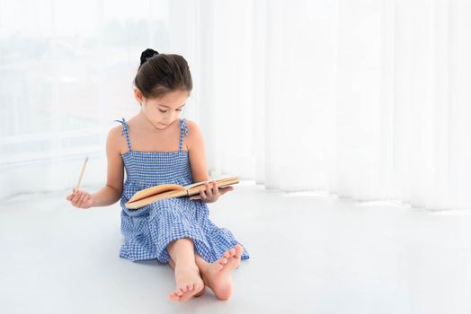 Cute girl reviewing homework and lessons with notebook and wooden pencil in hand in white bedroom background at home. Education and People lifestyles. Self-learning concept. Back to school theme.