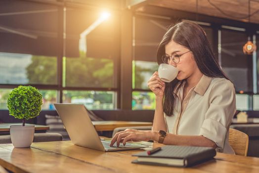 Asian working woman using laptop and drinking coffee in cafe. People and lifestyles concept. Technology and business theme. Freelance and occupation theme. Workaholic in overnight concept.