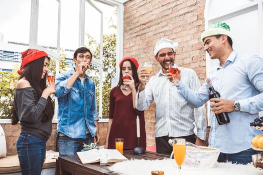 Outdoor Xmas party shot of young people toasting drinking glass at a rooftop terrace as forever friendship. Young friends hang out with alcohol drinking and juice. Christmas and New year party theme.