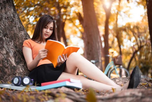 Asian beauty woman reading book in park. People lifestyles and Entertainment concept. Relaxation and Vacation concept. Autumn and fall seasonal theme.