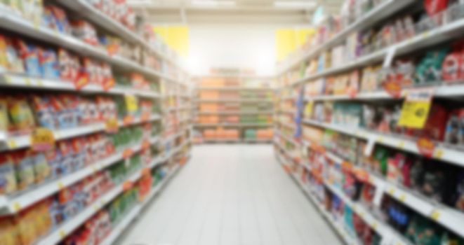 Blurry shopping shelves in supermarket and department store. Shopping mall product showcase walkway in front of shopping cart
