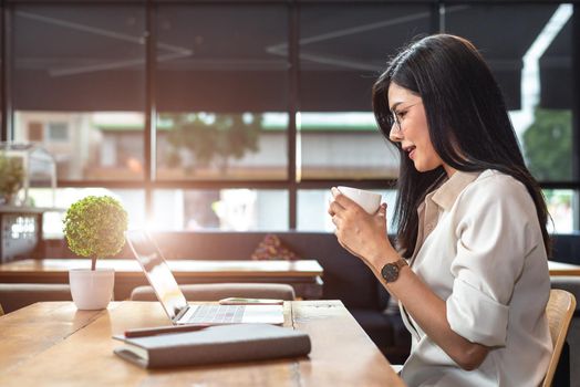 Asian working woman using laptop and drinking coffee in cafe. People and lifestyles concept. Technology and business theme. Freelance and occupation theme. Workaholic in overnight concept.