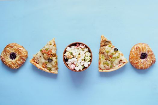 Slice of cheese pizza on a plate , donuts and popcorn on blue.