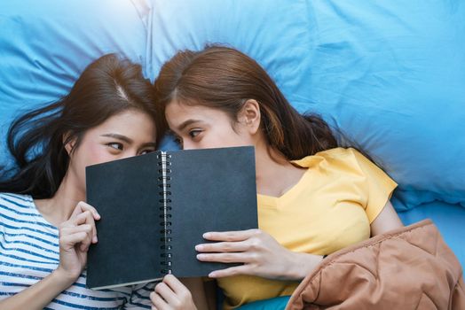 Cute Asian lesbian couple reading book together and lying on bed. Lifestyles and lovers concept. Happiness life and relax theme.