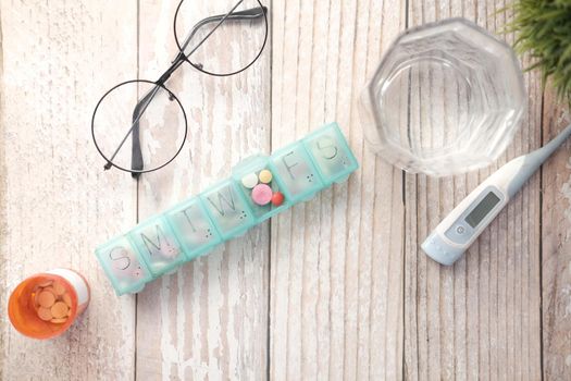 pill box, thermometer, container and glass of water on table .