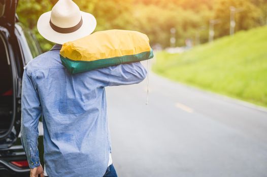 Back view of tourist walking along road with bag during travel in countryside. People lifestyles and vacation concept. Man holding and backpack for long holiday trip with mountain background