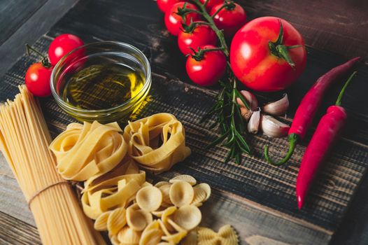 Tasty appetizing italian spaghetti pasta ingredients for kitchen cuisine with tomato, cheese parmesan, olive oil, fettuccine and basil on wooden brown table. Food Italian recipe homemade. Top view